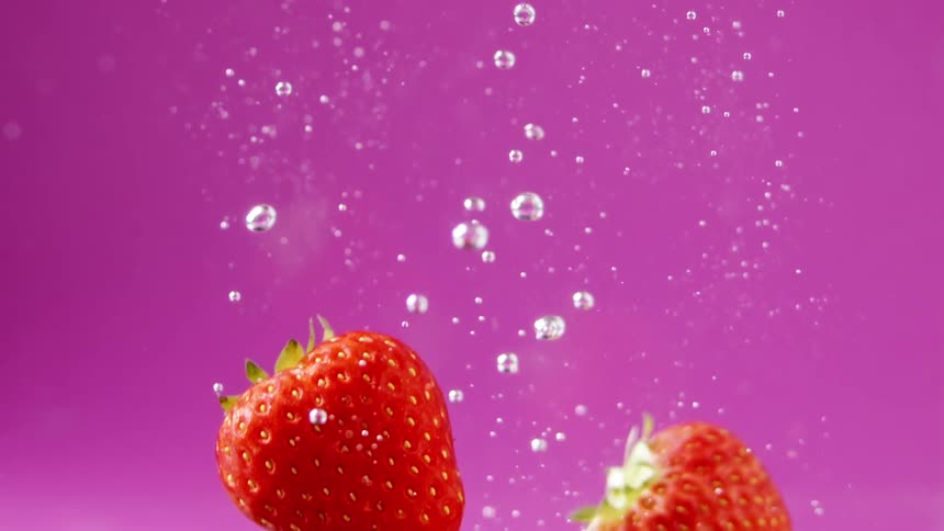 Strawberries falling underwater in front of a pink background