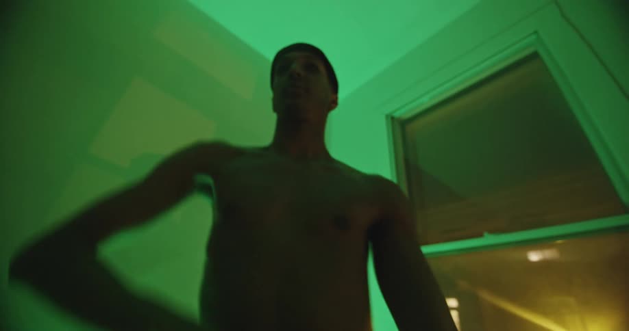 Shirtless man dances wildly in green lit room at night