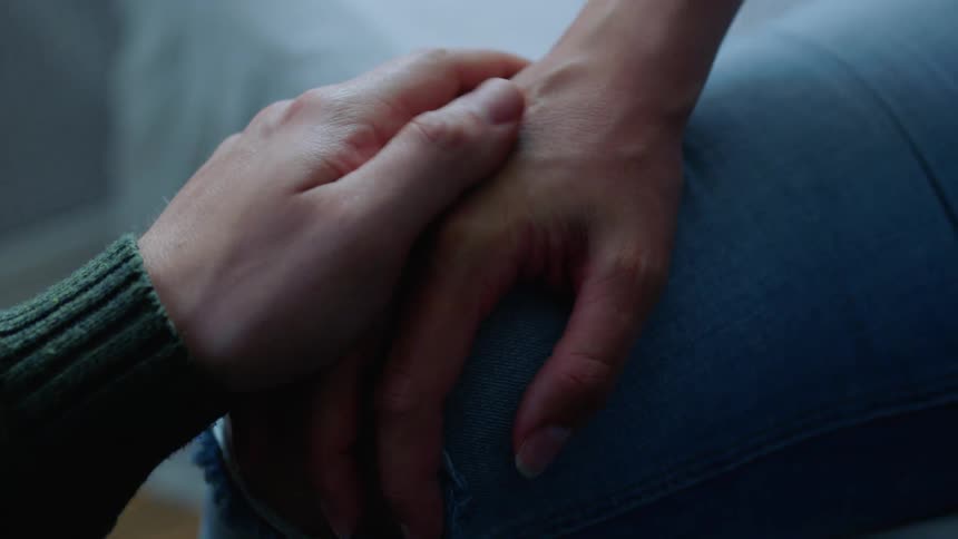 Close up of a man holding the hand of a woman in a consoling manner in a room