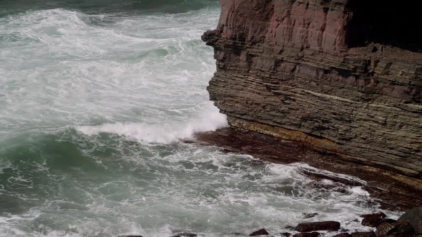 Ocean waves crash on the rocks of a steep cliff