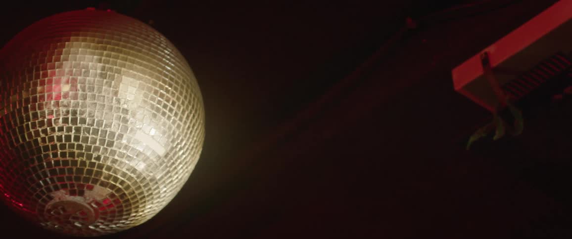 A mirrored disco ball spins and reflects light in a dark room