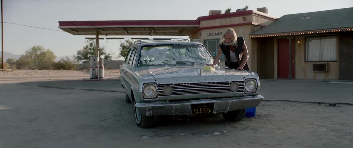 An old man hand-washes a car at a desert gas station.