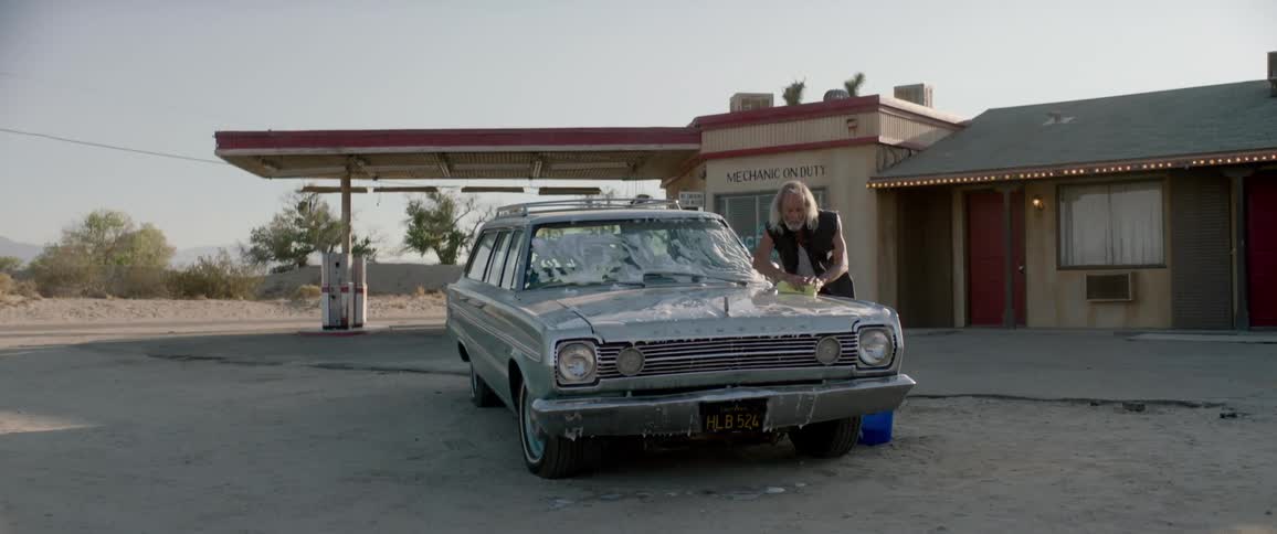 An elderly man hand-washes his car outside a gas station in the desert.