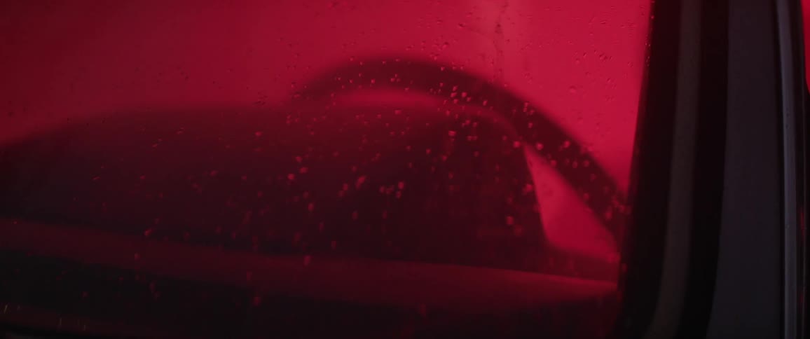 raindrops fall on a windshield of a car, glowing red from inside