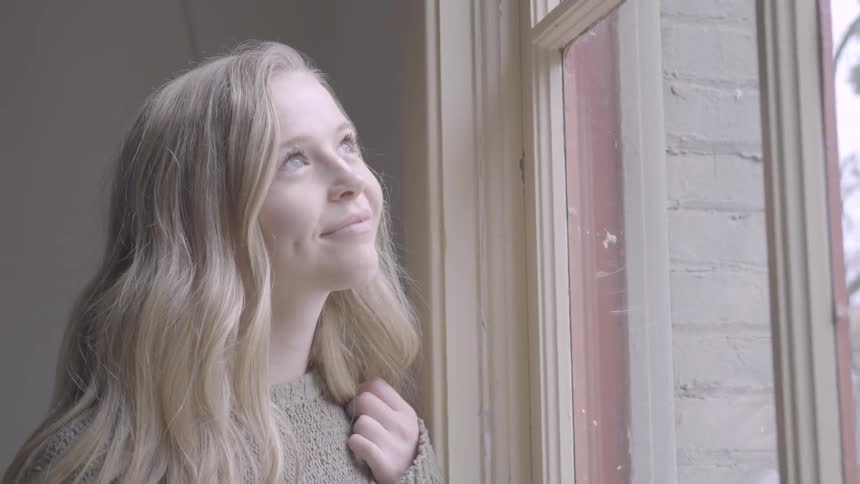 Blonde teenage girl with a brown pullover smiles and looks out the window
