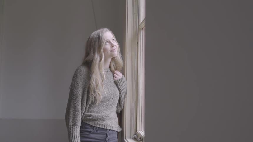 A young woman smiles while gazing out of a large window during the day