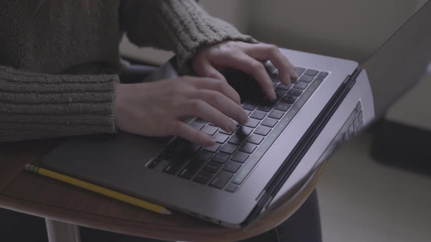 A student is typing on a laptop in a classroom