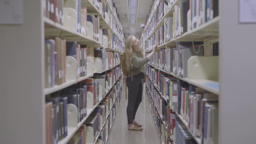 A young woman returns a book to a bookshelf in a library