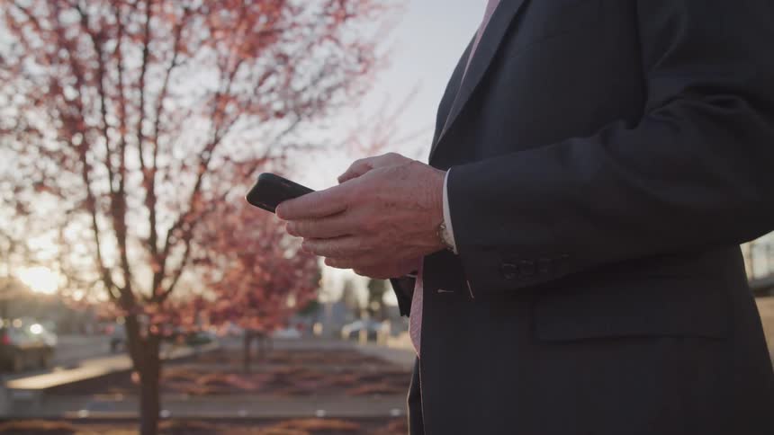 A man is standing outdoors and looking at a cellphone