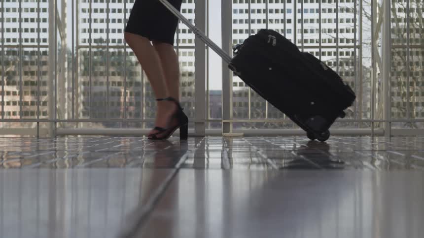 A woman walks through a building pulling a suitcase behind her
