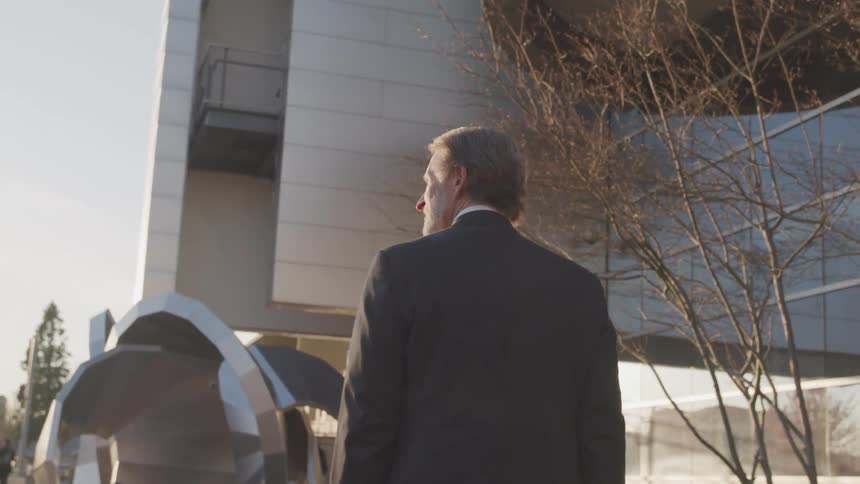 A man with a suit walking by an office building with the sky in the background