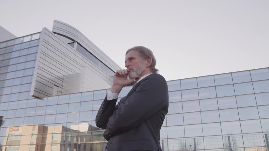 Businessman deep in thought stands in front of an office building