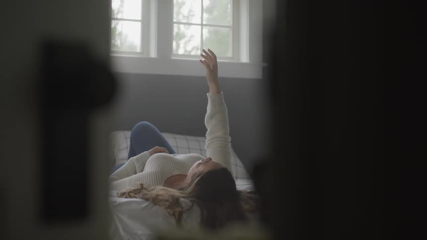 A teenage girl lying in bed with her arm stretched up towards the ceiling