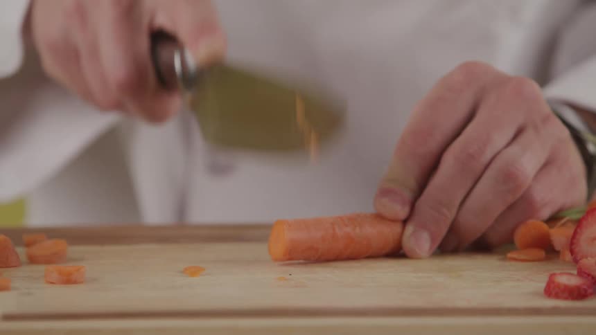 Chef uses a knife to chop up a carrot in slices as they prepare for a meal dropping knife when they are done