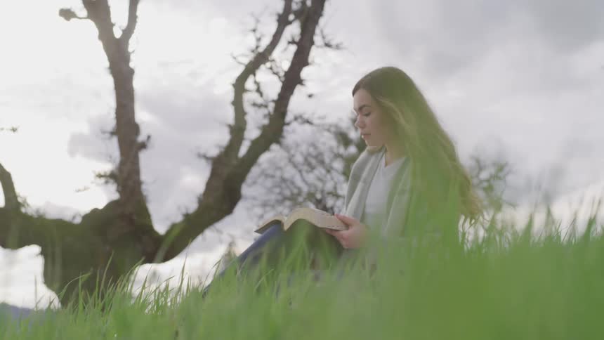A woman is reading a book while sitting outdoors