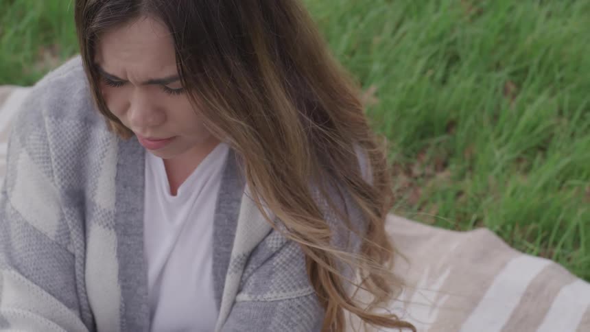 A teenage girl sitting outside on a blanket looking sad