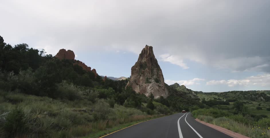 A vehicle drives by a large rock formation on a cloudy day