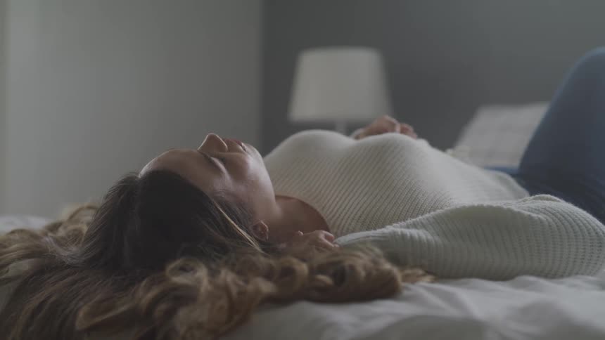 A young woman lays on her back on a bed while relaxing