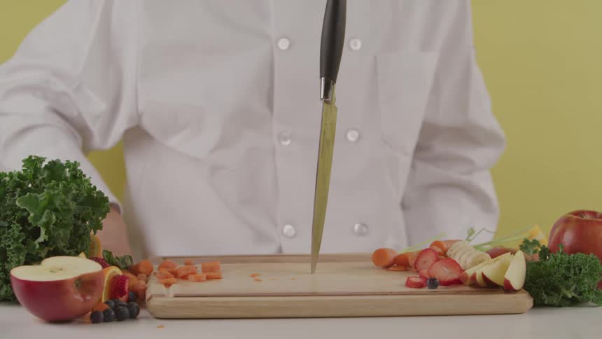 A chef stabs a knife in to a cutting board with cut up fruit on it
