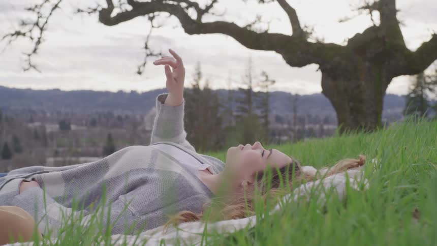 A woman is laying on a blanket in the grass