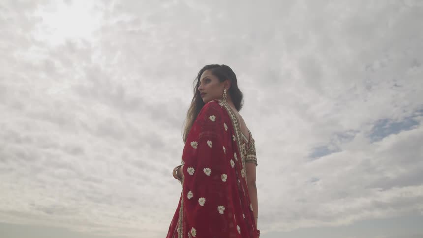 Hindu woman wearing traditional clothes and a bindi in her forehead stands pensively on the beach