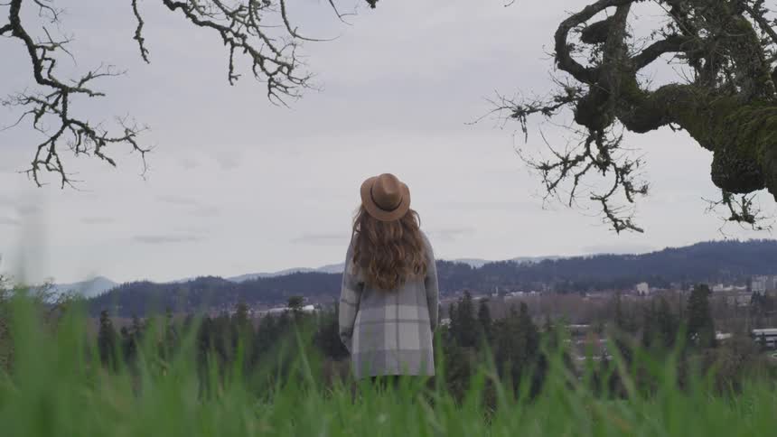 Woman wearing a plaid coat looks out at a distant forest