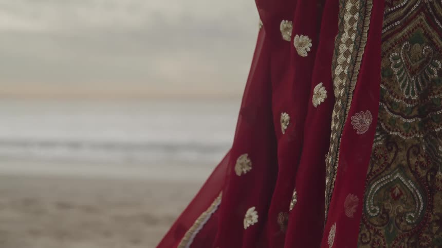 A person covered with cloth on the beach with the ocean and the sky in the background