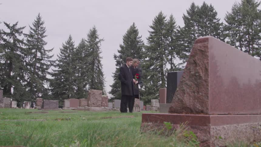 Couple mourns in front of a gravestone in the cemetery near the pine trees