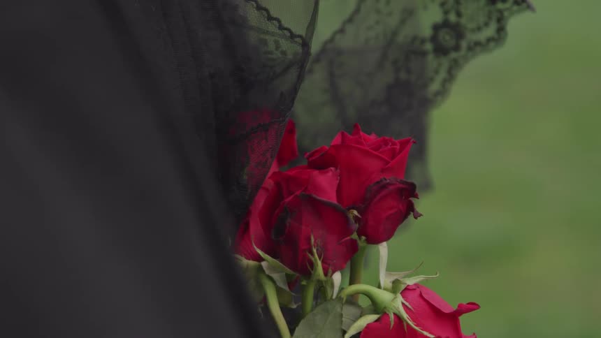 A person in a black veil holding red roses while mourning