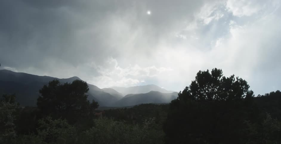 The sun shines through clouds over mountains