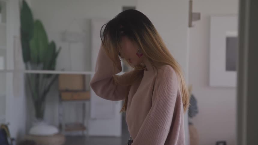 A young asian woman runs her fingers through her hair as she walks through a house
