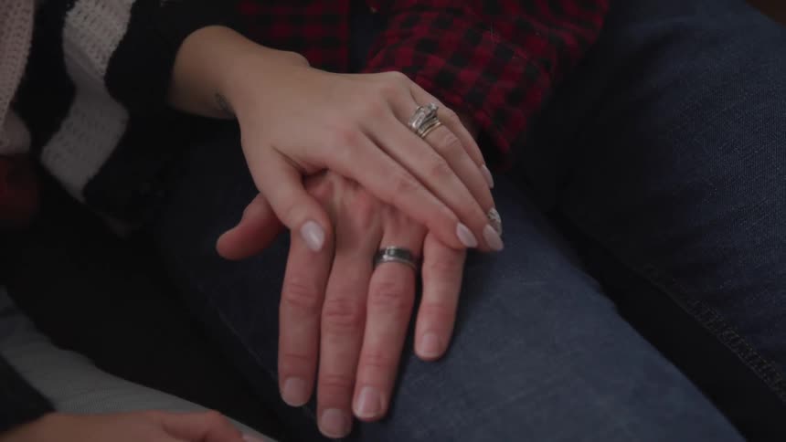 A man with his hand on his wifes leg as she rubs his hand