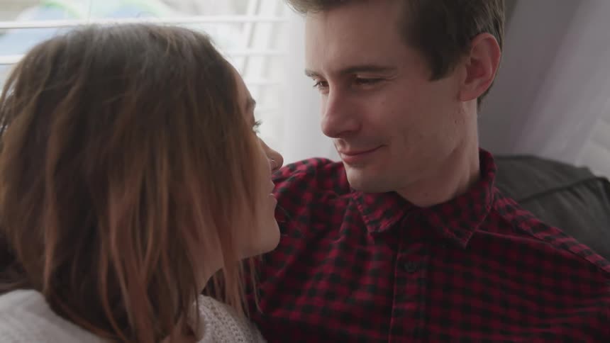 Man with a red striped shirt and woman with a sweater look into each others eyes with affection in the living room
