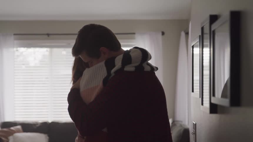 Man and woman look into each others eyes and cuddle one another with affection in a room