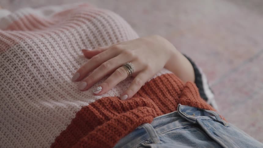 Woman wearing a ring resting on the floor rest her left hand over her torso
