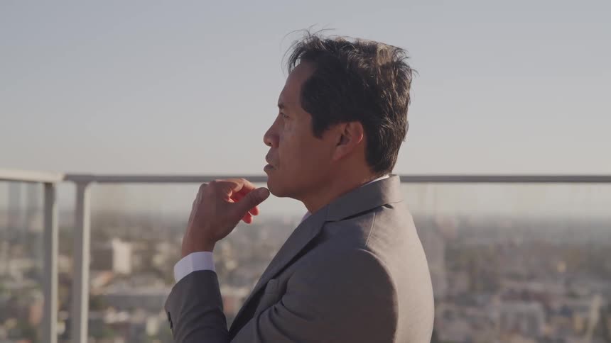 Business man stands near rail looking out over urban sprawl