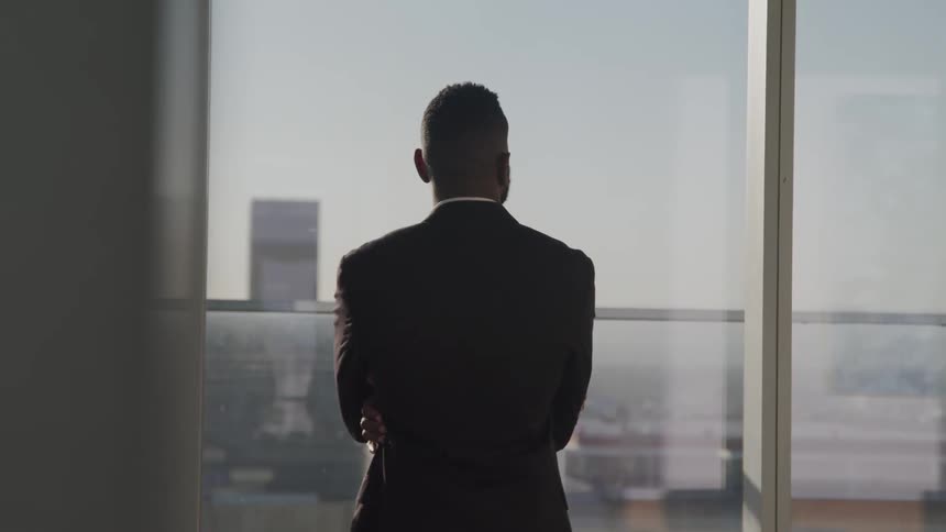Businessman with a black suit looks out the office windows in the office