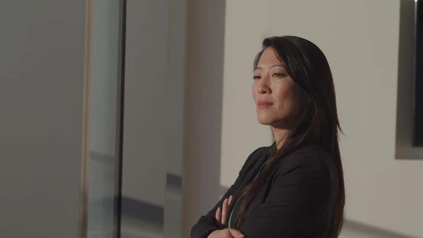 Asian businesswoman with a black blazer looks out the office windows