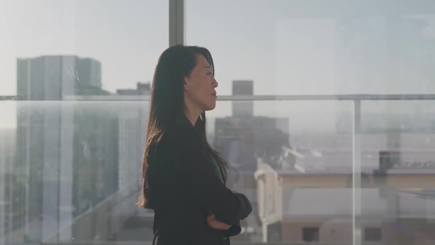 Business woman walks pensively on an office in a penthouse of a skyscraper on the city at sunset