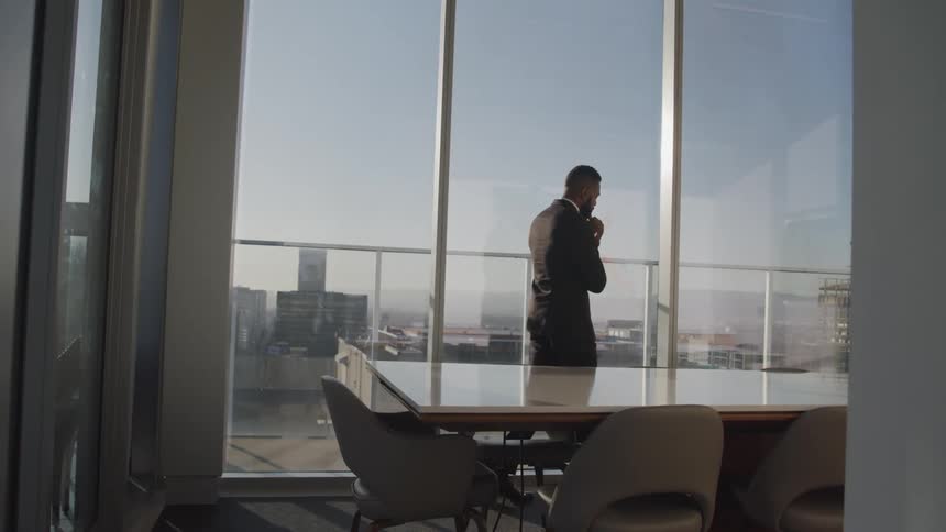 A man in a suit and tie walking in a conference room with a table and chairs