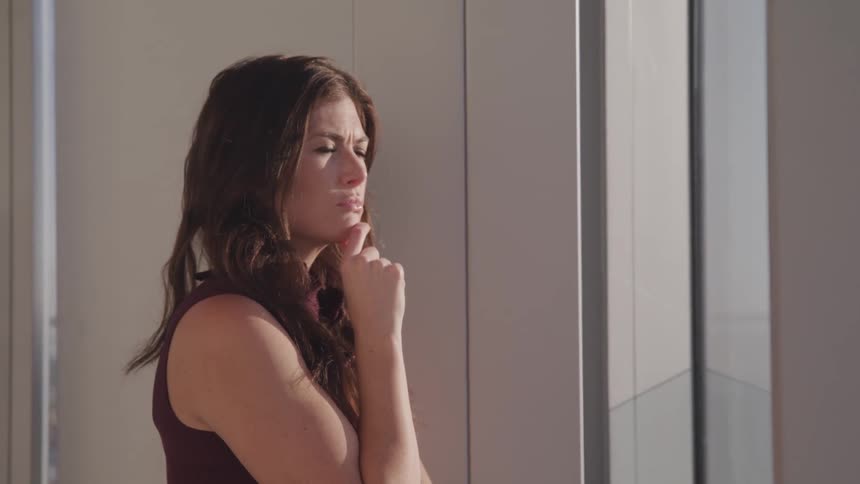 A woman is standing indoors and looking out a window