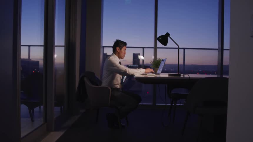A male asian sitting at a desk in an office typing on a keyboard