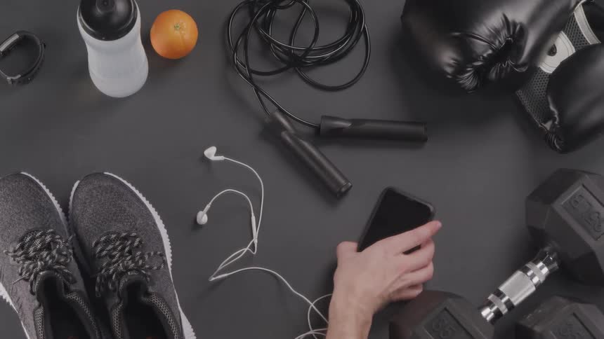 Person picks up sneakers and mobile phone from among other exercise and sports equipment