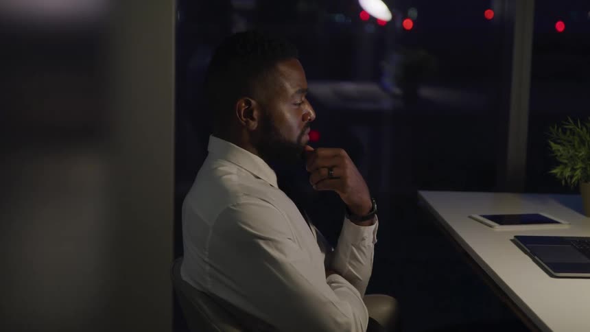 A man sitting at a desk in front of a laptop with a window in the background