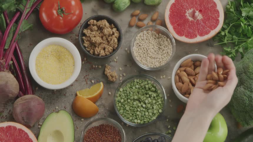 A person takes a handful of nuts from a table covered in fruits and vegetables and shakes them in their palm