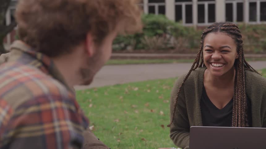 Three people sitting on grass talking and laughing