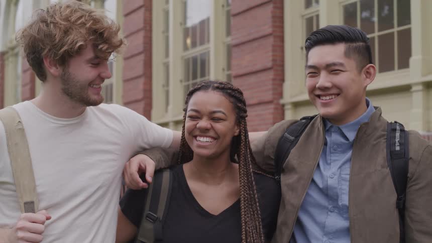 Students stand in front of building with arms around each other smiling and laughing