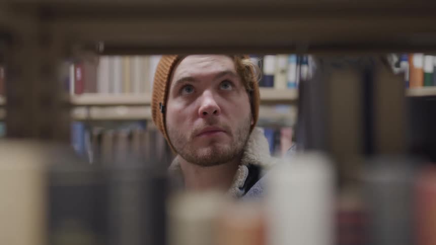A man examines the books on a bookshelf in a library