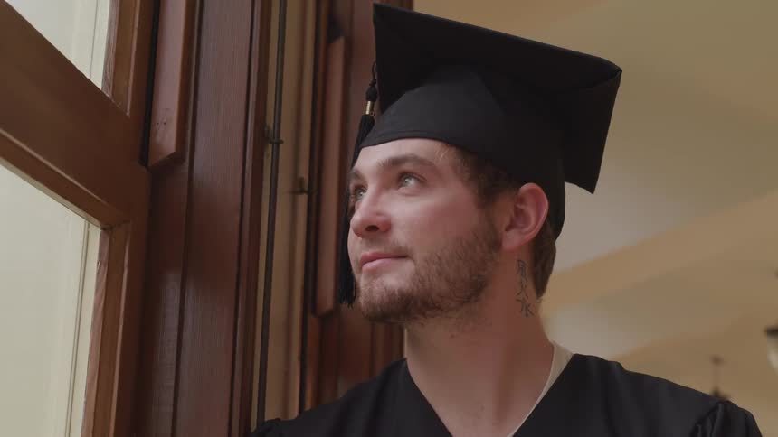 A graduate is smiling as he looks out the window