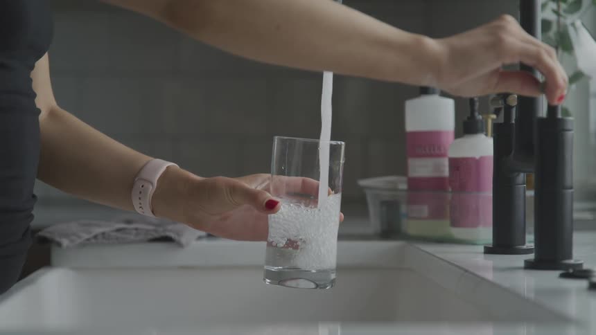 A woman is at the sink filling a glass with water